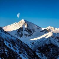 Snow Covered Mountain Peak with Crescent Moon and Blue Sky photo