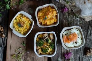 Mini casseroles featuring broccoli with cheddar, mushrooms with sun-dried tomatoes, and egg with salmon on a wooden table photo