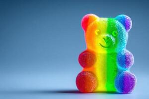 A brightly colored gummy bear figurine features a rainbow gradient of colors. The bear has a friendly expression and is placed on a smooth surface, highlighting its playful design. photo