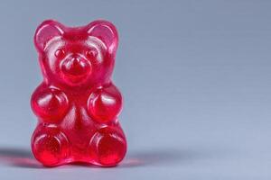 A vibrant red gummy bear stands upright against a smooth gray backdrop. Its glossy surface reflects light, showcasing its cheerful shape and texture, inviting a sense of nostalgia and joy. photo