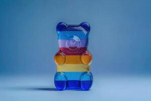 A vibrant gummy bear is displayed prominently, showcasing a mix of colors including red, orange, yellow, and blue against a soft blue background. The bear appears glossy and inviting. photo
