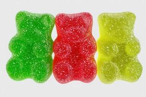 Three gummy bears in green, red, and yellow colors are arranged side by side. Their shiny surfaces sparkle, showcasing their sugary texture, perfect for candy enthusiasts. photo