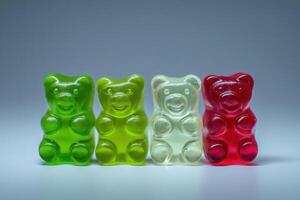 Four gummy bear candies in vibrant colors of green, yellow, and red are aligned on a smooth surface. The bright hues highlight the playful and fun nature of these popular sweets. photo