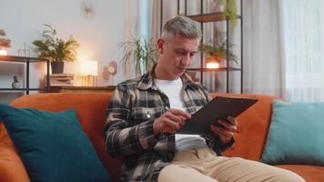 homem lendo papel documentos revendo relatórios, calcular custos, rendimentos, despesas, trabalhando às casa video