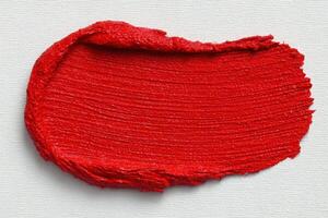 A bold red paint stroke is spread smoothly across a textured canvas background, showcasing a rich and glossy finish. The vivid color highlights the dynamic potential for artistic creation. photo