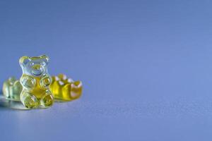 A vibrant gummy bear and other candy shapes sit on a smooth, light surface. The playful arrangement highlights their different colors and textures, inviting a sense of fun and indulgence. photo