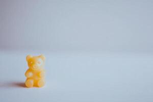 A small yellow gummy bear is prominently displayed against a smooth surface. Soft lighting creates a gentle ambiance, highlighting the bears cheerful features and texture. photo