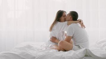 A young couple expresses love and affection while sitting on a neat bed. Soft light filters through sheer curtains, creating a warm, intimate atmosphere suitable for relaxation and connection. video