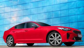 Red car against the blue sky with white clouds reflected in a glass building. Stylish, modern, bright image of a car for design solutions. photo