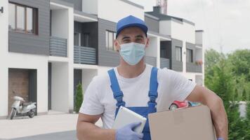Portrait of young mailman courier wearing mask and gloves, who is delivering a parcel directly to a customer home with safety. Home delivery in quarantine video