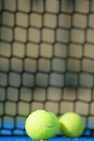 two padel balls near the net in a blue paddle tennis court, net blurred background photo