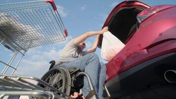 Adult Man with disabilities in a wheelchair puts purchases in the trunk of a car in a supermarket parking lot 5 video