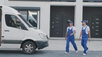 Two young workers of removal company unload boxes and furniture from minibus into customer's home 8 video