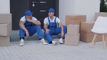Two removal company workers have a break while sitting on the step 4 video