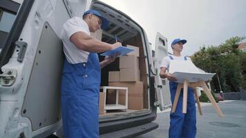 Two young workers of removal company unload boxes and furniture from minibus into customer's home 20 video