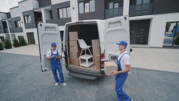 Two young workers of removal company are loading boxes and furniture into a minibus 59 video