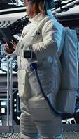 Vertical Portrait of cheerful astronaut holding helmet inside high tech spacecraft, holding equipment case during routine mission check. Jolly woman in starship standing near monitor showing Mars data video