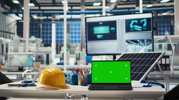 Green screen laptop in photovoltaics factory for monitoring performance of robot arms. Chroma key digital device in empty industrial facility used to inspect solar plant machines video