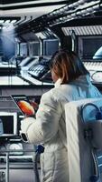 Vertical Cheerful astronaut holding helmet doing human expansion in space using spacecraft. Happy african american woman in starship prepares for expedition supporting long term mankind survival, camera A video