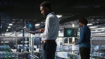 Server hub teamworking IT experts visualizing large language model architecture using notebook. Data center system administrators on industrial platform collaborating on tasks using laptop video