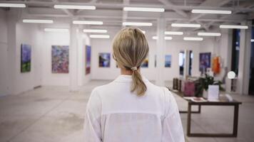 A young woman in casual attire explores a contemporary art gallery, where urban art spaces invite public engagement with vibrant paintings. video