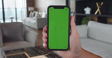 Close up smartphone with green chroma key mockup screen in with vertical position at home background. Male hold smartphone in hand with chroma key green screen at living room. Chromakey mock-up. video