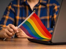 Rainbow flag showing in hand while sitting at the table in the office photo