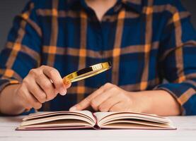 Close-up of hand holding a magnifying glass and reading a book while sitting at the table photo