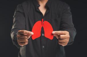 A man holding a lung shape symbol while standing on a black background. photo