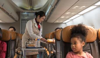 Flight attendant in beige uniform with red scarf serves meal to passenger on airplane. photo