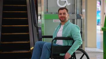 Portrait of smiling person with disability sitting in wheelchair near elevator in mall video