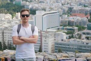 A man tourist with a backpack at the background of the panorama of the city of Athens at the observation deck. Front view. Travel touristic concept photo