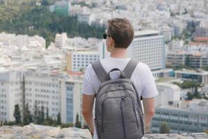 A man with a backpack looks at the panorama of the city of Athens from the observation deck. View from behind. Travel touristic concept photo