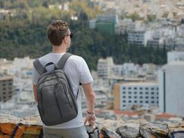 A man tourist with a backpack looks at the panorama of the city of Athens from the observation deck. View from behind. Travel touristic concept photo