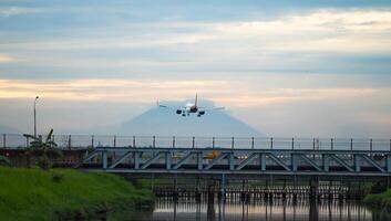 Airplane landing over a bridge and river at sunset with mountain silhouette photo