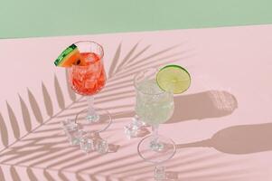 Summer scene with refreshing watermelon and lime drinks and palm leaves shadow on pink and green background. Sun and shadows. Minimal cocktail concept. Trendy summertime party idea. Summer aesthetic. photo