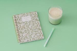 Trendy layout made with iced matcha latte, notebook and pen on pastel green background. Minimal creative concept. photo