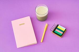 Colorful layout with pink notebook, green iced matcha latte and yellow pen on purple background. Minimal creative concept. photo