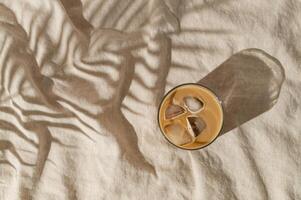 Summer day scene made with iced coffee and tropical palm tree leaf shadow on sand color linen background. Sun and shadows. Minimal summer coffee concept. Flat lay style. Top view. photo
