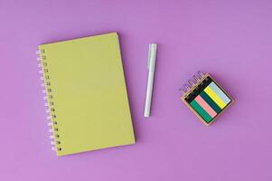 Green spiral notebook and pen on a vibrant purple background. Trendy composition ideal for creative workspaces, office themes or back to school concepts. Minimalistic colorful office desk flat lay. photo