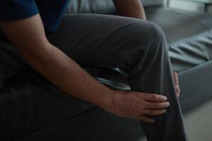 Leg pain, a man sitting on a couch with his knee in pain photo