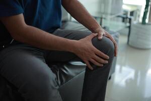 Knee pain, a man with knee pain sitting on a couch photo