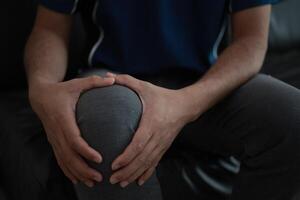 Closeup of a man sitting on a couch with his knee in pain photo