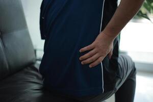 a man with back pain sitting on a couch photo