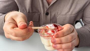 A Caucasian man savors a rustic wooden spoon of strawberry swirl yogurt, reminiscent of Nordic Midsummer and quirky small indulgences photo