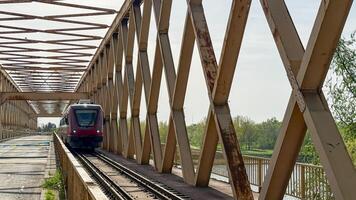 Red train glides through iron lattice, echoing nostalgic transit dreams, bridging Arbor Day serenity and Railroad Enthusiasts Month photo