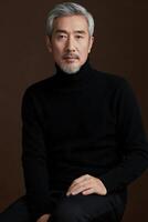 An asian man in a black turtle neck sweater sitting on a brown chair photo