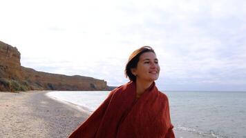 A woman in a red blanket is standing on the beach video