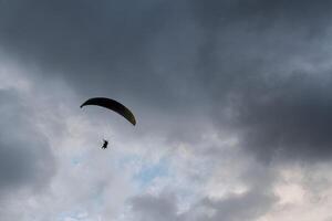A paraglider soars against a dramatic sky filled with dark and light clouds. photo