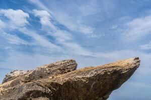Two jagged rock protrusions stand prominently against a blue sky filled with feathery white clouds. photo
